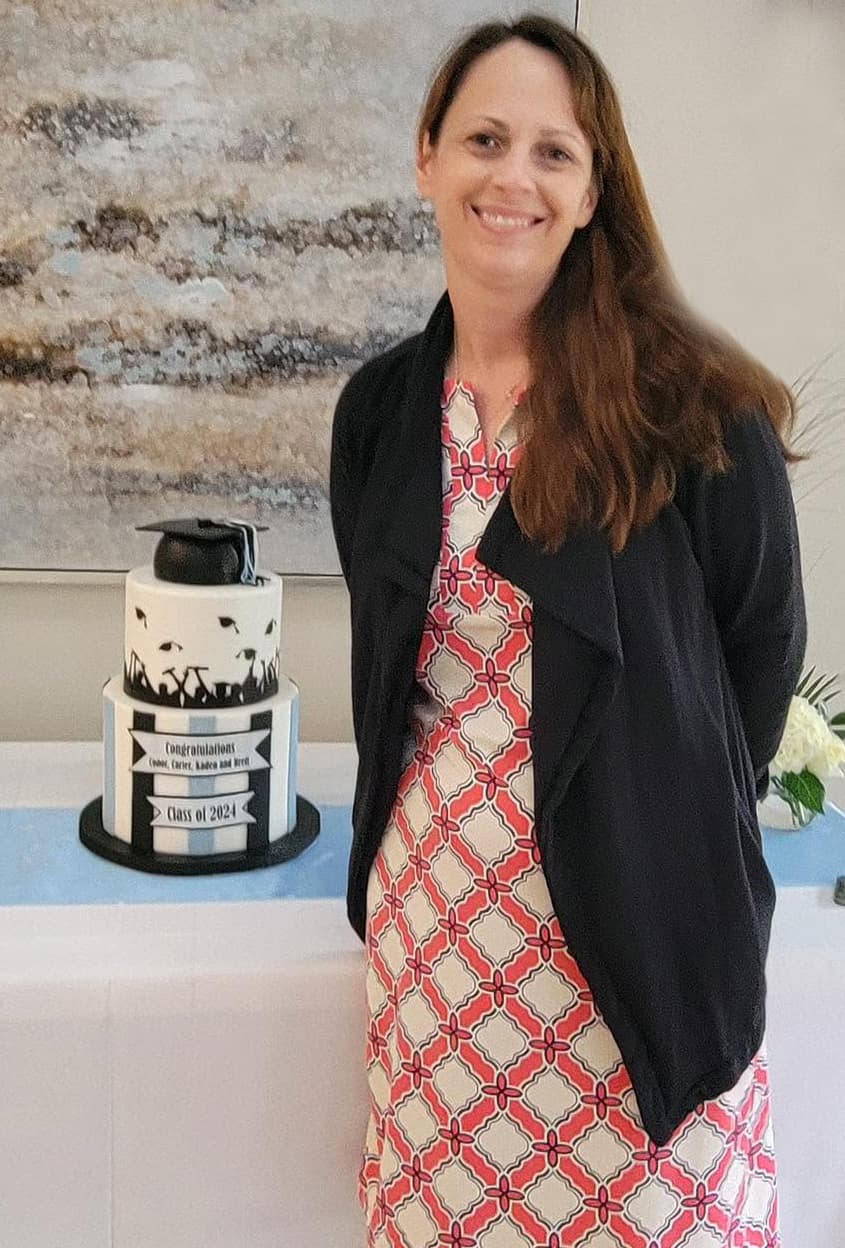 Kristen, the baker and cake artist behind Sweet Cakes by Kristen, standing beside a custom graduation cake