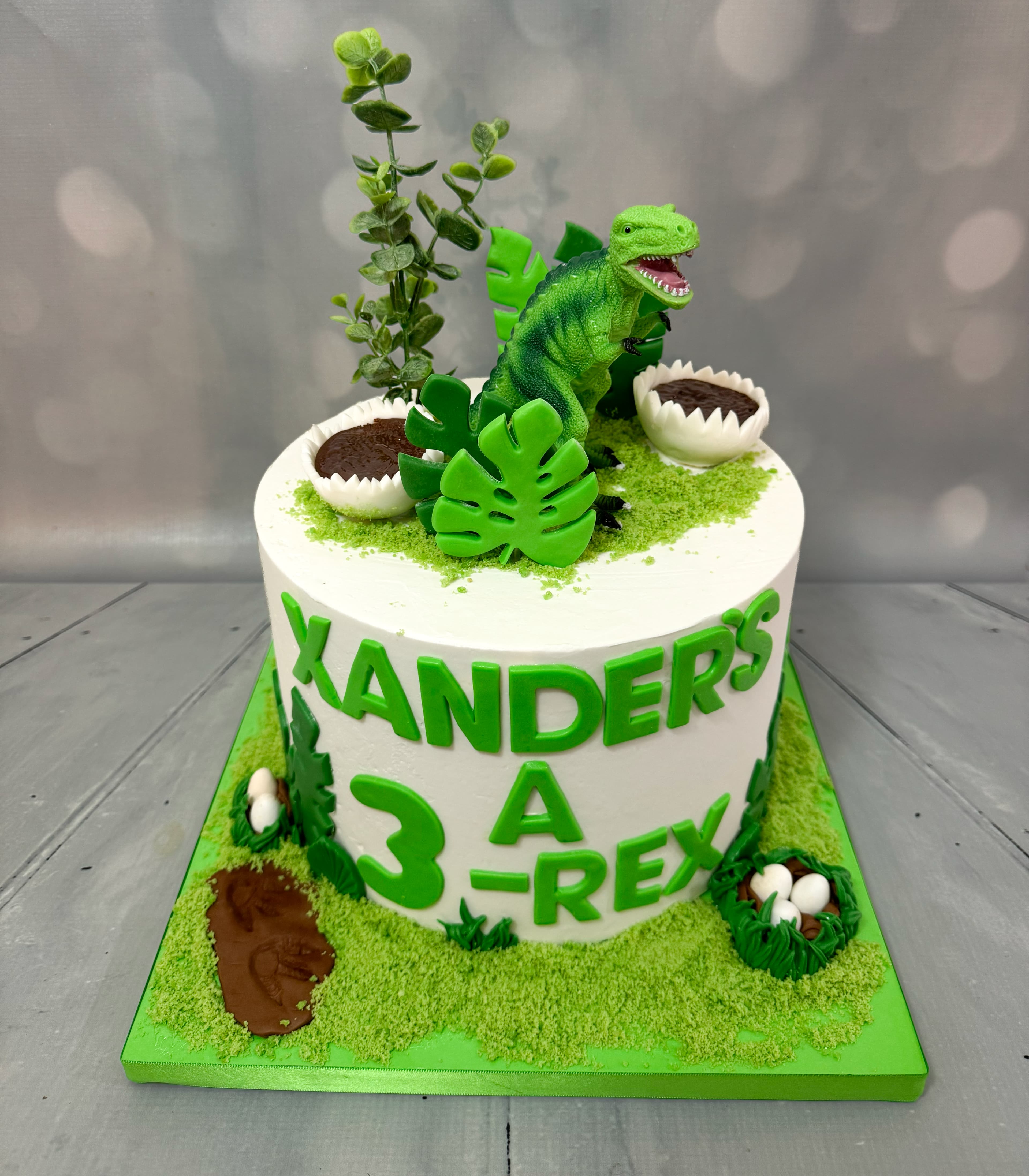 Three-Rex dinosaur birthday cake with green dinosaur and tropical decorations by Sweet Cakes by Kristen